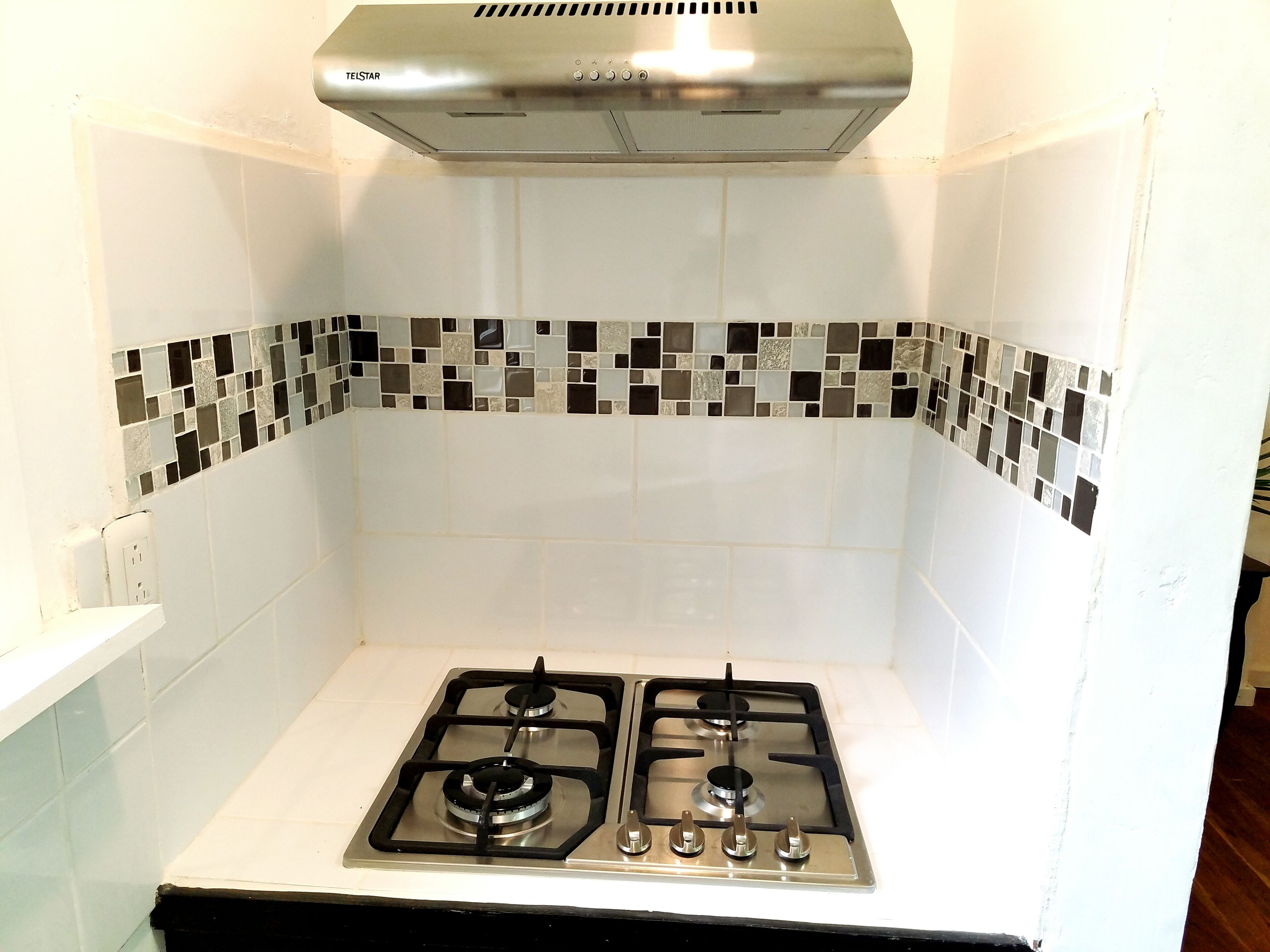Una cucina con due fornelli a gas, una cappa aspirante in acciaio inossidabile e un backsplash piastrellato con motivo a mosaico.