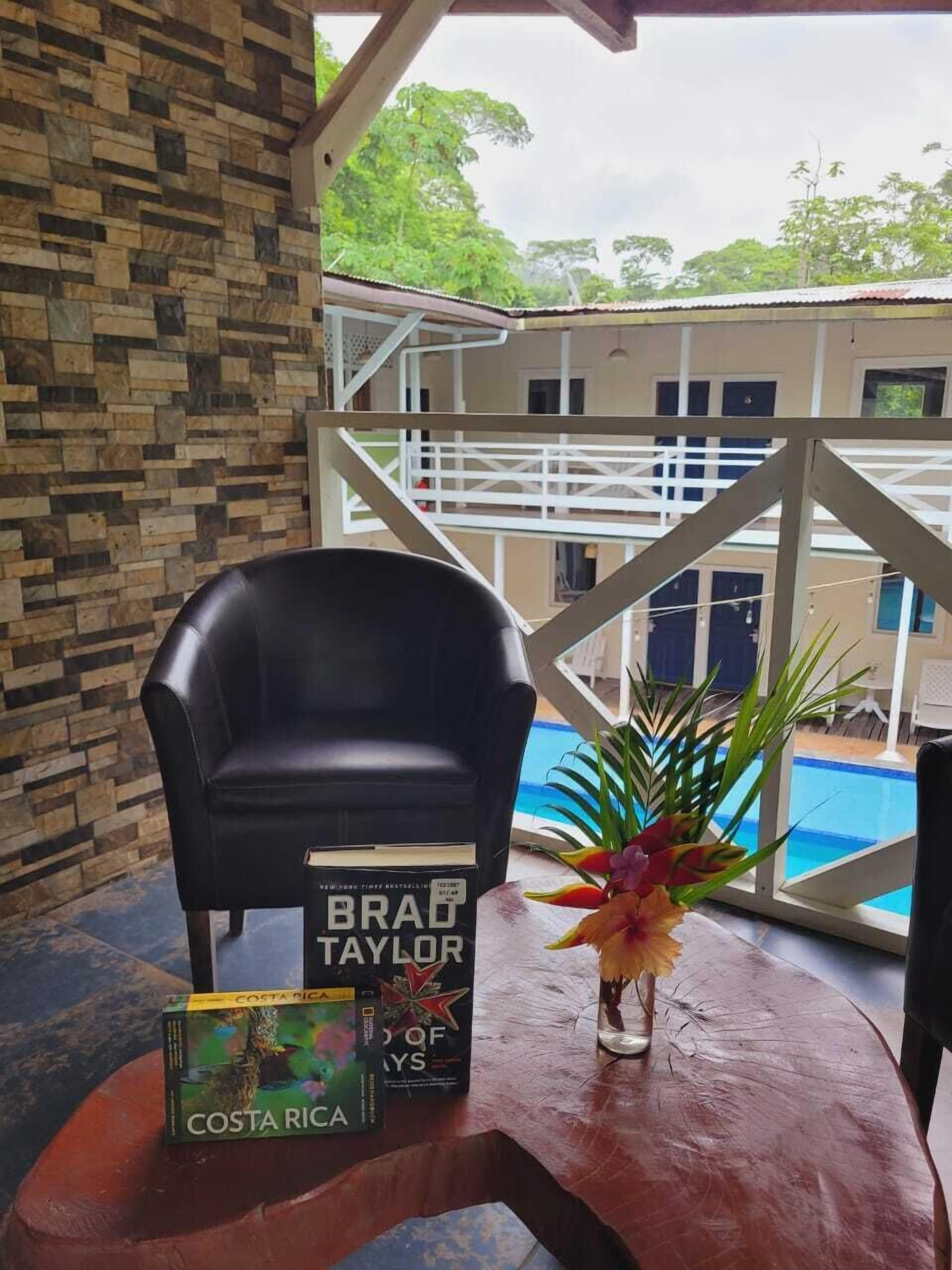 A room with a black leather chair, a table with a book titled 'Costa Rica,' and a vase with flowers.