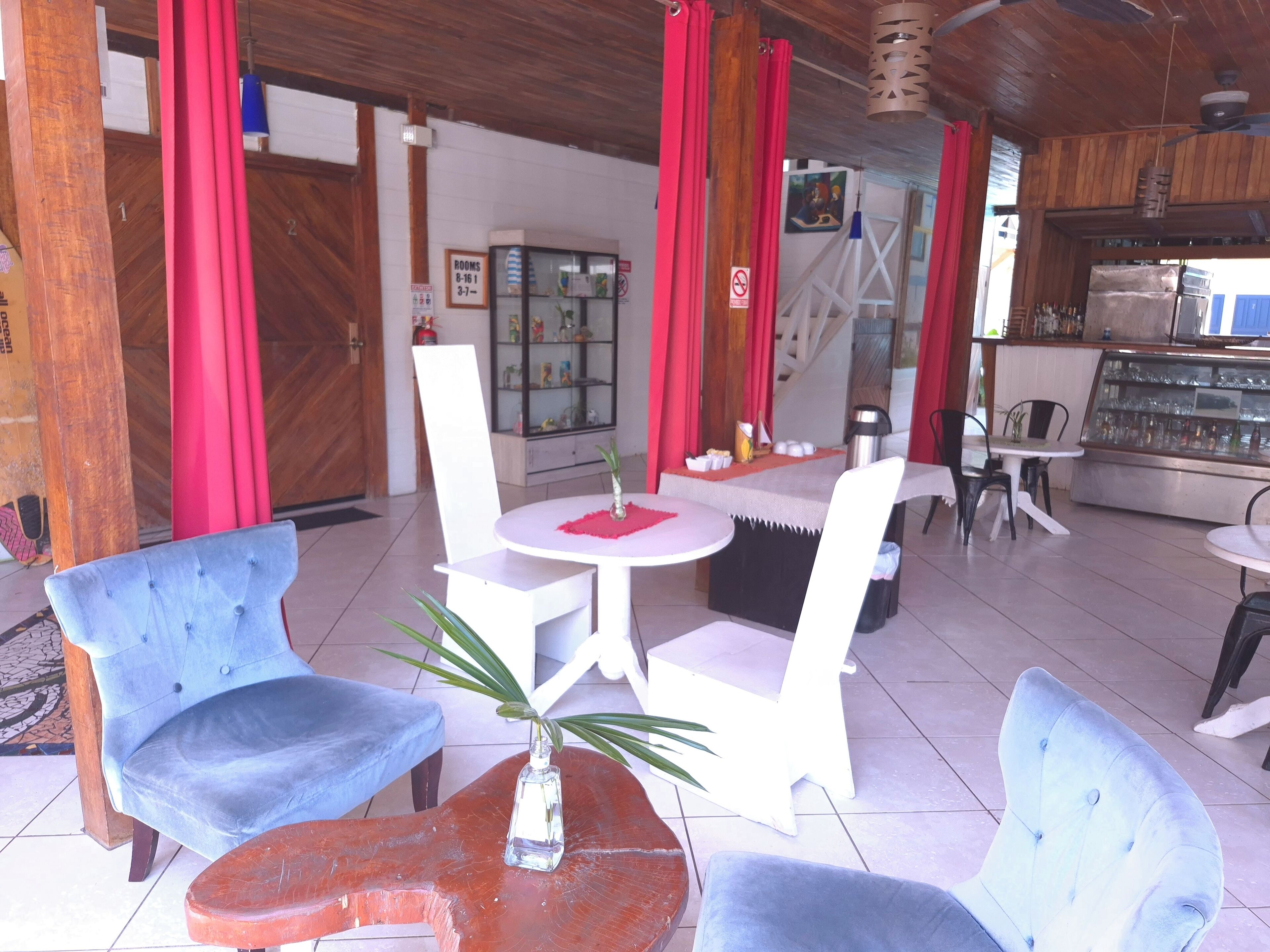 A restaurant with round tables and blue chairs, a glass display case, and red curtains.