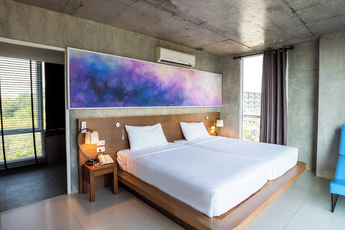 A modern hotel room with a large bed, bedside lamps, a blue chair, and a large abstract painting on the wall.
