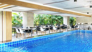 A poolside area with tables and chairs, a pool, and a view of greenery.