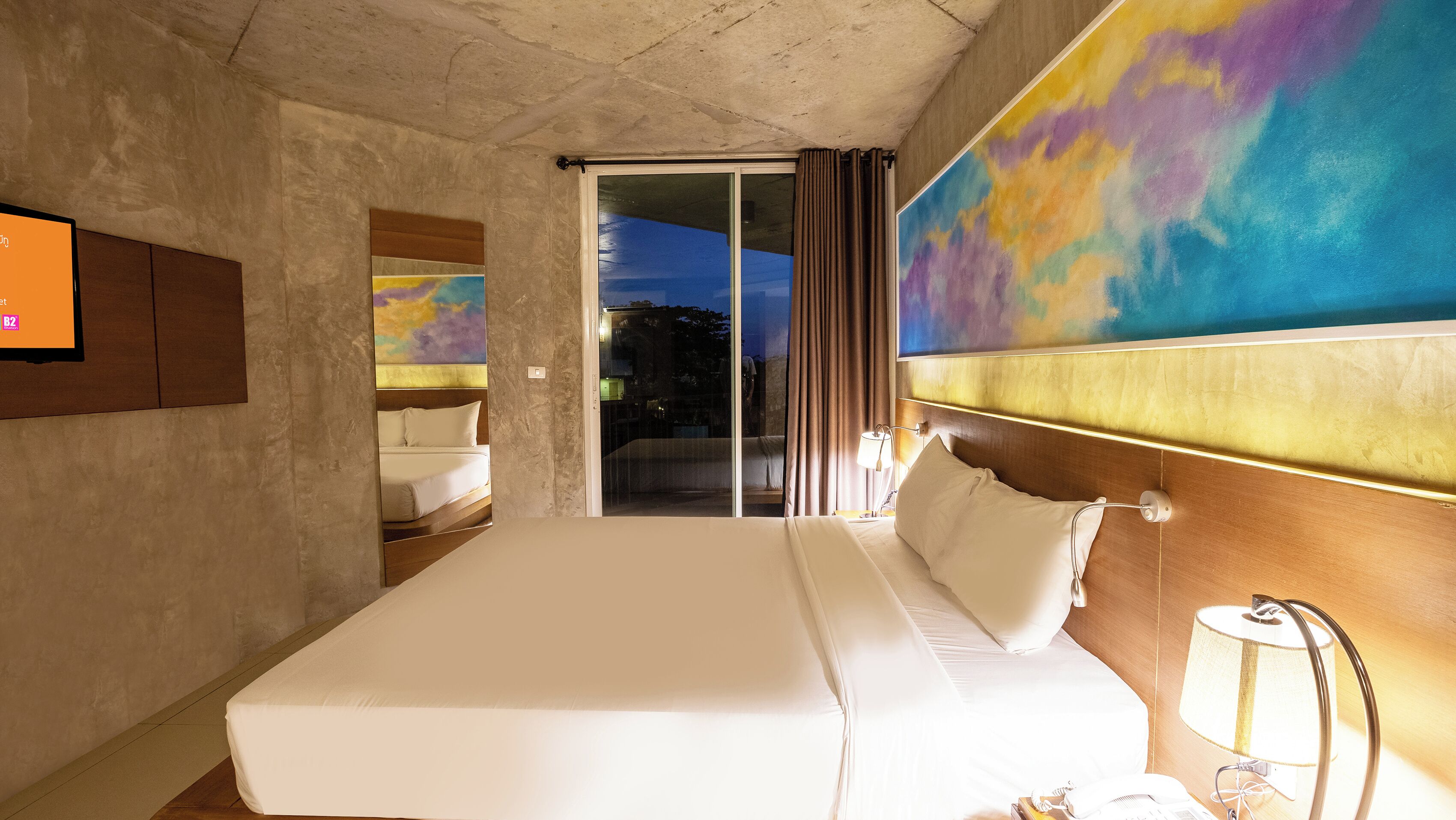 Een hotelkamer met een groot bed, een aan de muur bevestigde televisie en uitzicht op de omgeving door een schuifdeur.