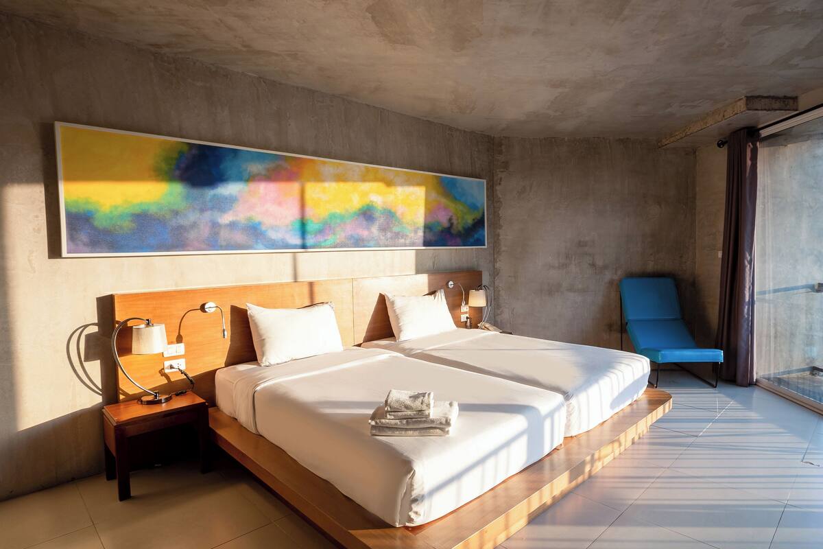 A modern hotel room with a large bed, a blue chair, and a balcony with a view.