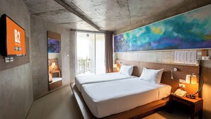 A hotel room with two beds, a large abstract painting, a TV, and a balcony with a view.