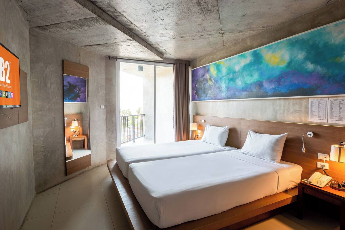 A hotel room with two beds, a large abstract painting, a TV, and a balcony with a view.
