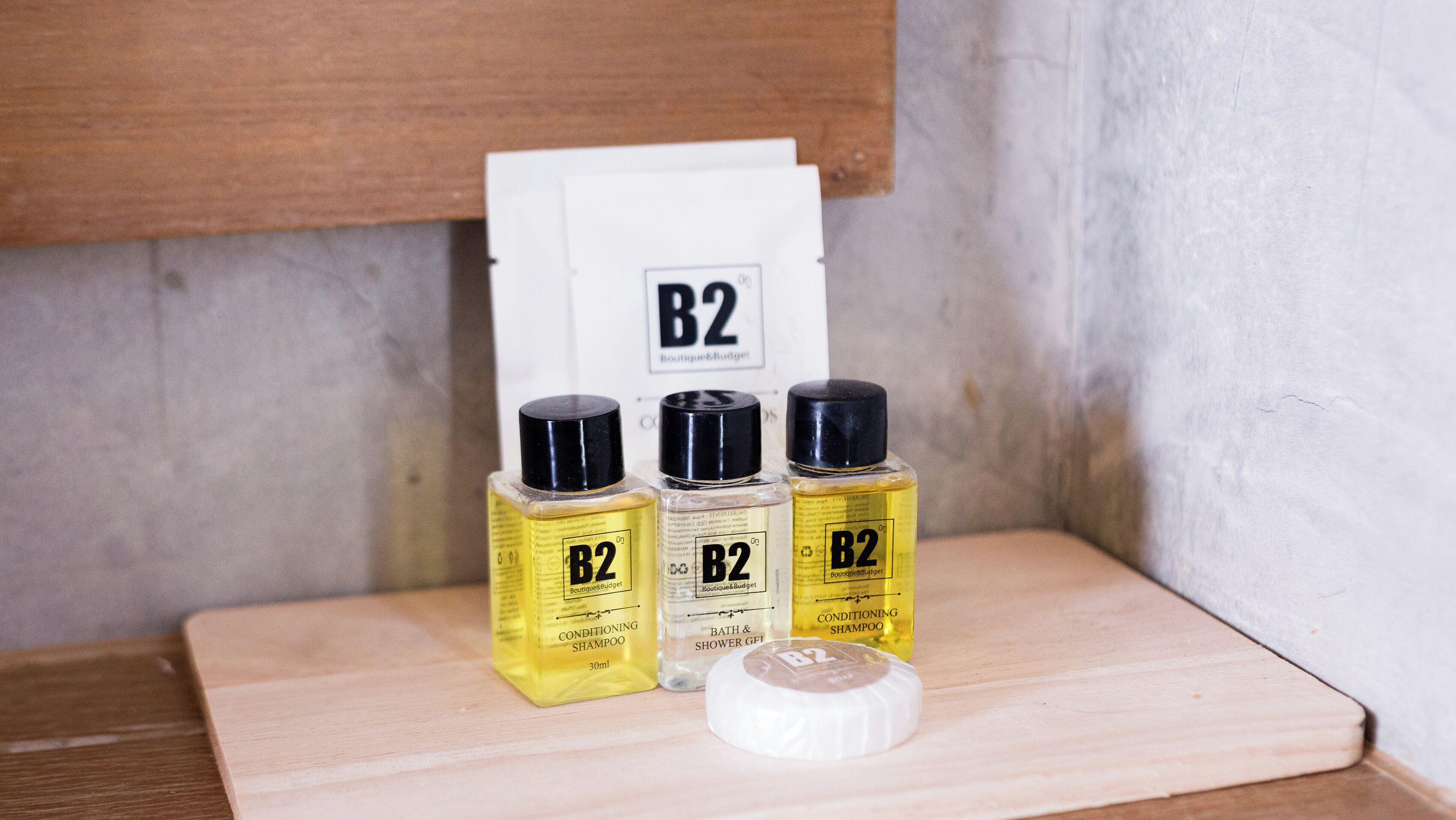Three B2 conditioning shampoo bottles, a bath & shower gift, and a white container on a wooden surface.