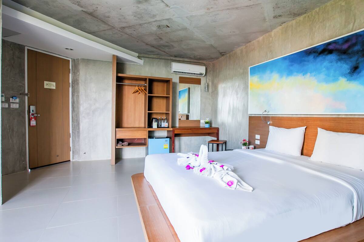 A hotel room with a large bed, a wooden headboard, a painting on the wall, and a desk with a chair.