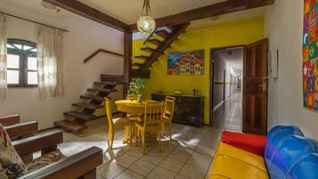 Uma área de refeições com uma mesa redonda e cadeiras, uma escada e um mural colorido na parede.