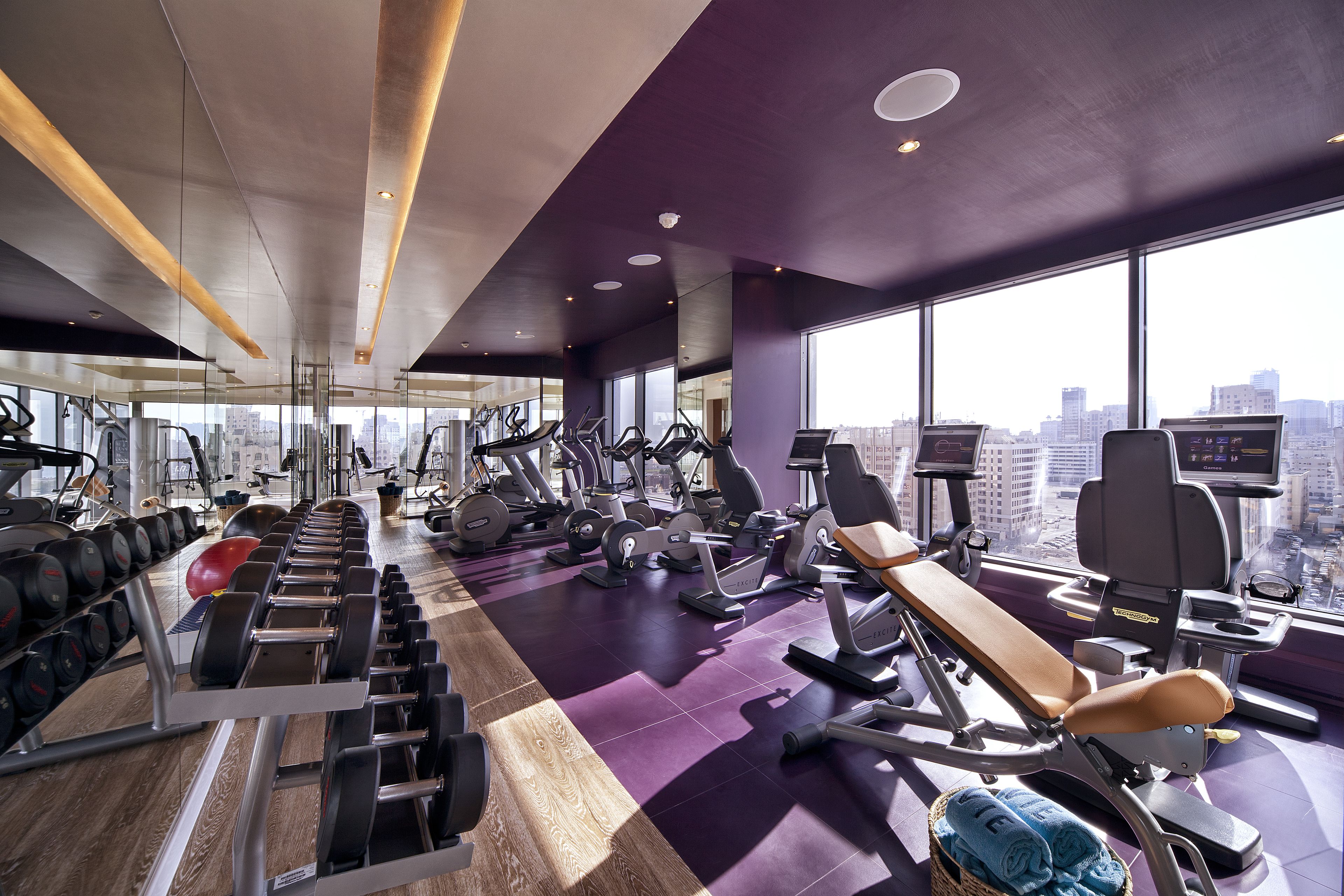 A modern gym with various exercise equipment, large windows, and a city view.