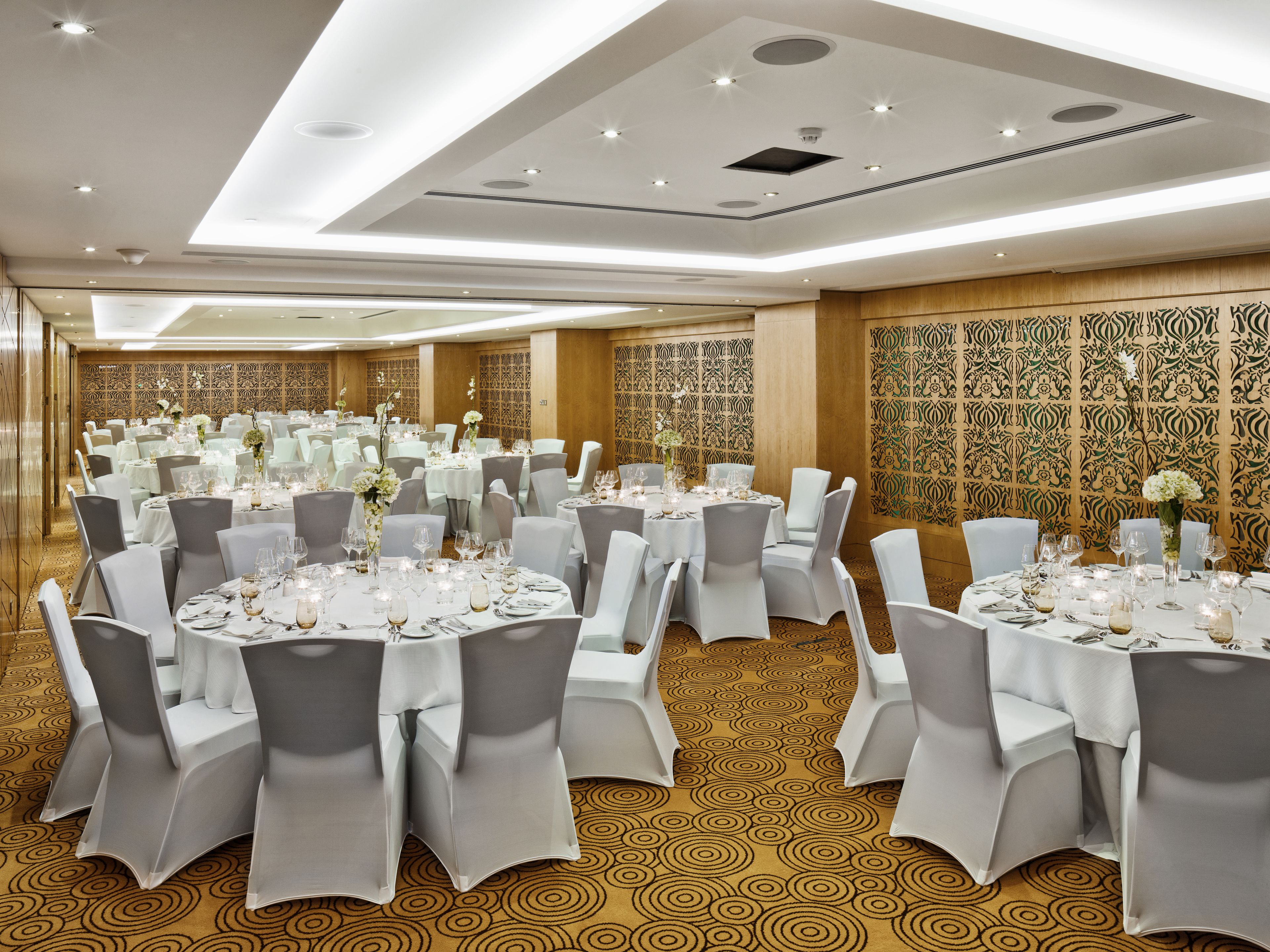 Un salón de banquetes con mesas redondas, sillas blancas y centros de mesa florales.