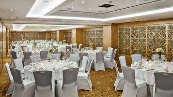 Un salón de banquetes con mesas redondas, sillas blancas y centros de mesa florales.