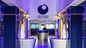 Ein Empfangsbereich mit modernem Design, der einen Empfangstresen, Vasen mit Zweigen und ein Schild mit der Aufschrift „IMARI“ zeigt.