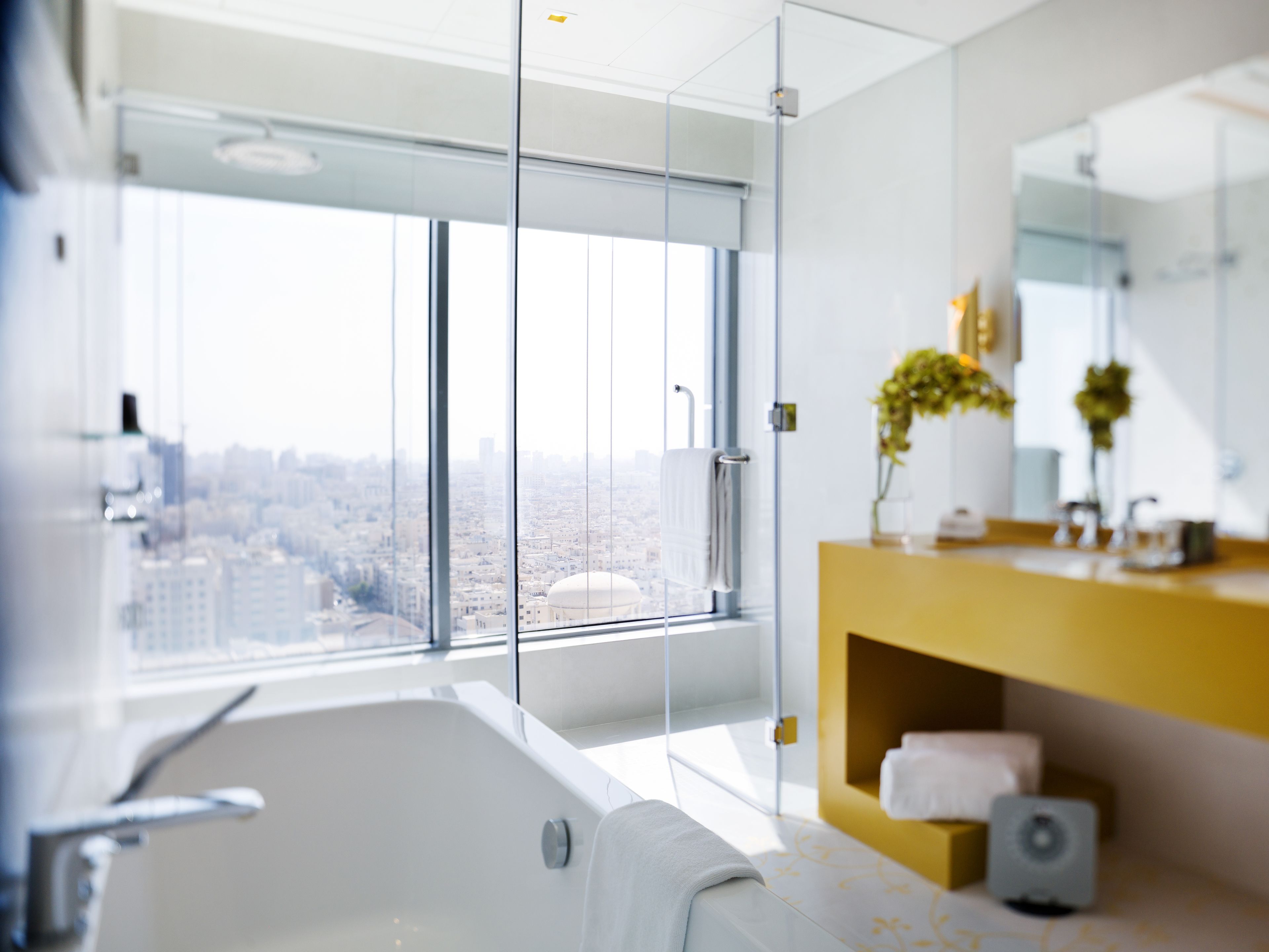 A modern bathroom with a large bathtub, a glass shower enclosure, and a city view.