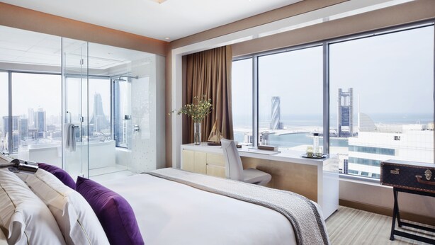 Ein modernes Hotelzimmer mit einem großen Bett, einem Schreibtisch und Blick auf die Stadt durch große Fenster.