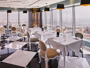 A modern dining area with tables set for service, large windows offering city views, and contemporary black pendant lighting. - The Domain Bahrain Hotel and Spa - Adults Friendly 16 Years Plus (Manama)