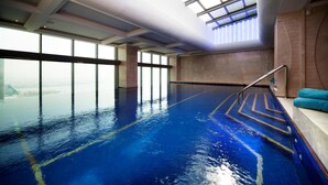 Ein überdachter Pool mit Glaswänden, einem blauen Boden und einer Treppe zu einer Sitzecke.