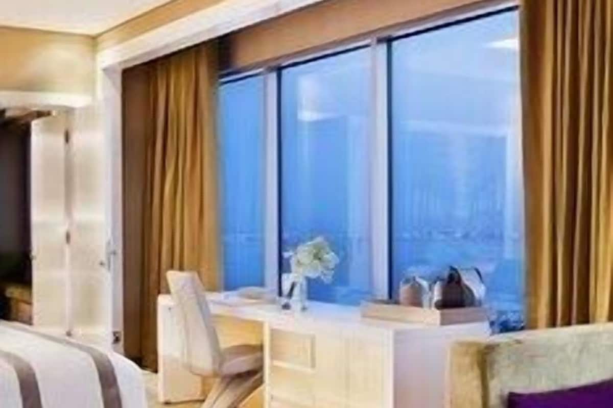 A modern hotel room with a bed, a desk, a chair, a sofa, and large windows.