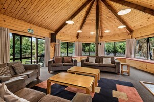 A spacious room with wooden ceilings, large windows, and multiple seating areas including sofas and a coffee table.