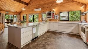 A spacious kitchen with wooden beams, a large island, white cabinetry, and a view of greenery outside. - Altamont Lodge (Wanaka)