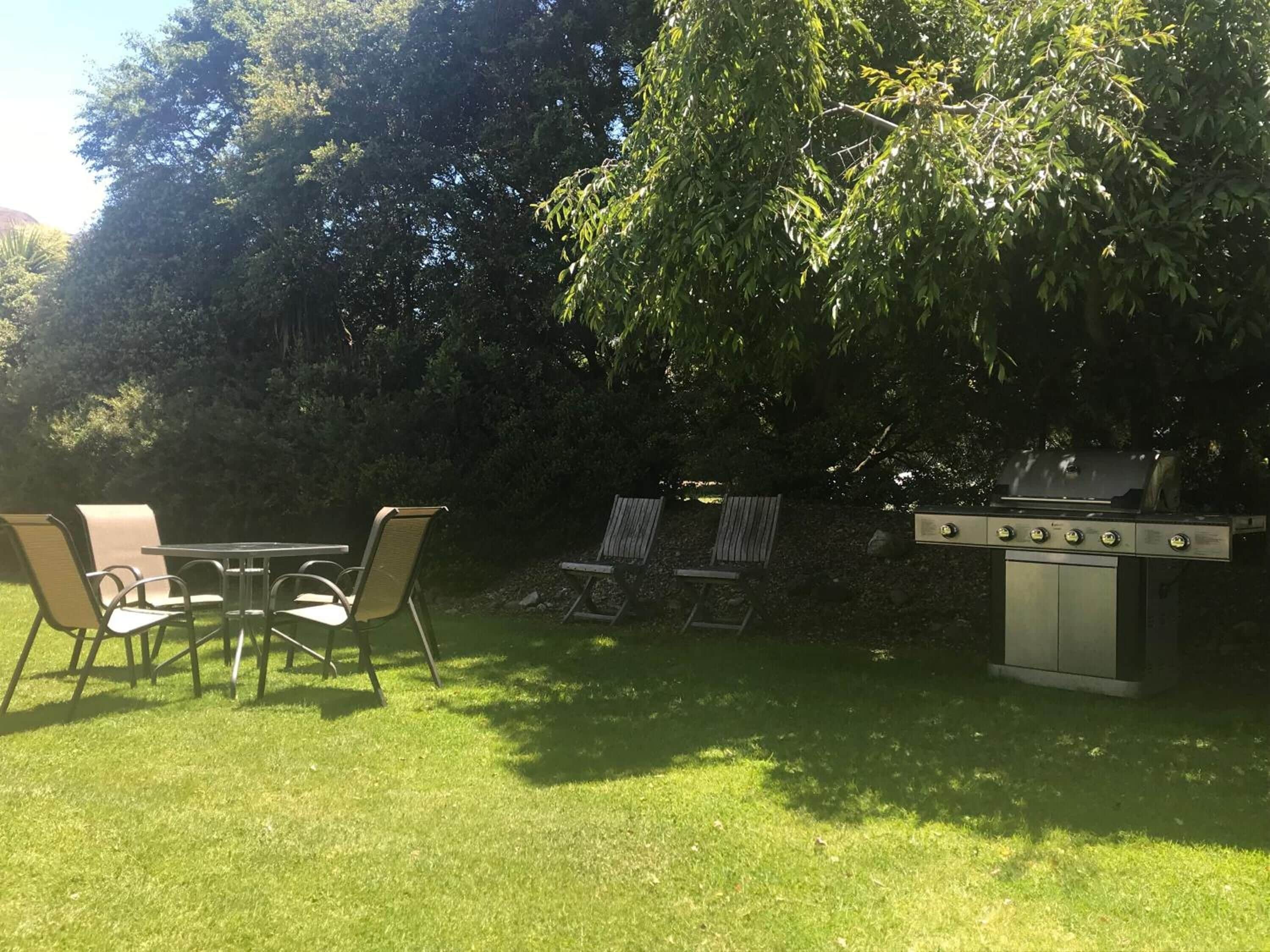Un patio al aire libre con una parrilla, sillas y una mesa.