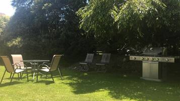 Un patio al aire libre con una parrilla, sillas y una mesa.