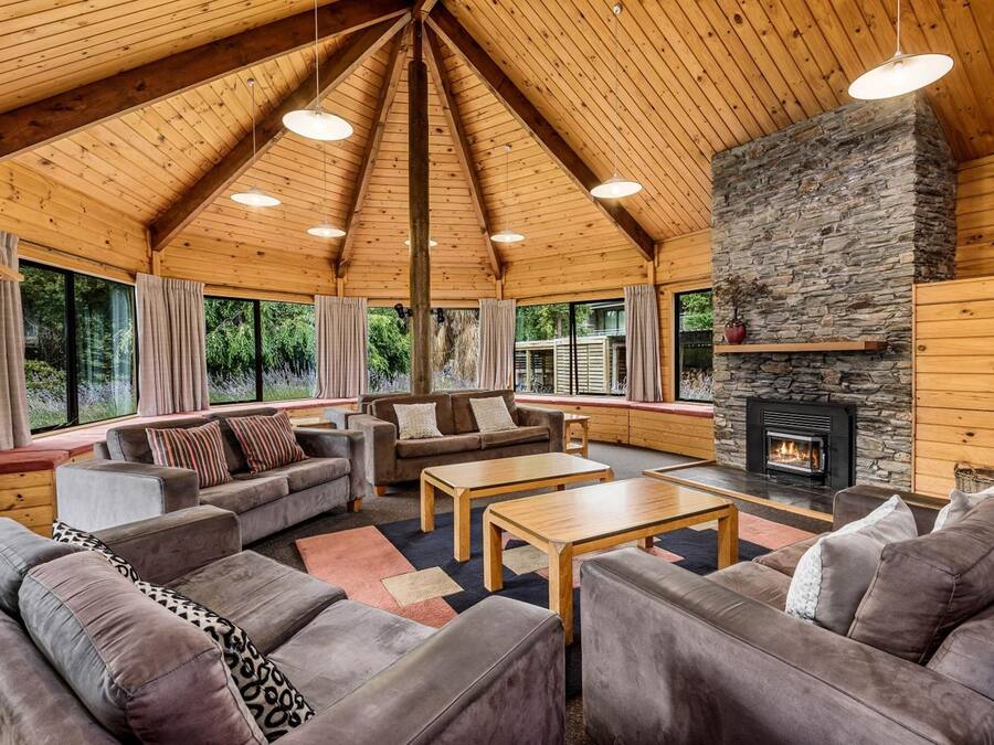 Interior acogedor de una cabaña con chimenea de piedra, techo de madera y grandes ventanales con vistas al bosque.