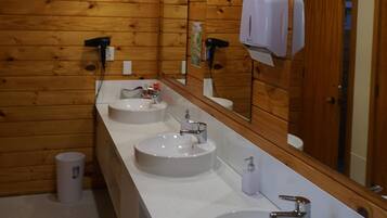 Une salle de bain de style rustique, avec des murs en bois, trois lavabos, un grand miroir et un sèche-cheveux.