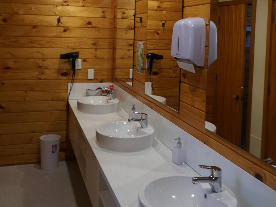 Une salle de bain de style rustique, avec des murs en bois, trois lavabos, un grand miroir et un sèche-cheveux.