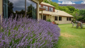 A two-story house with a large glass window, a well-maintained lawn, and a table with chairs in the backyard. - Altamont Lodge (Wanaka)