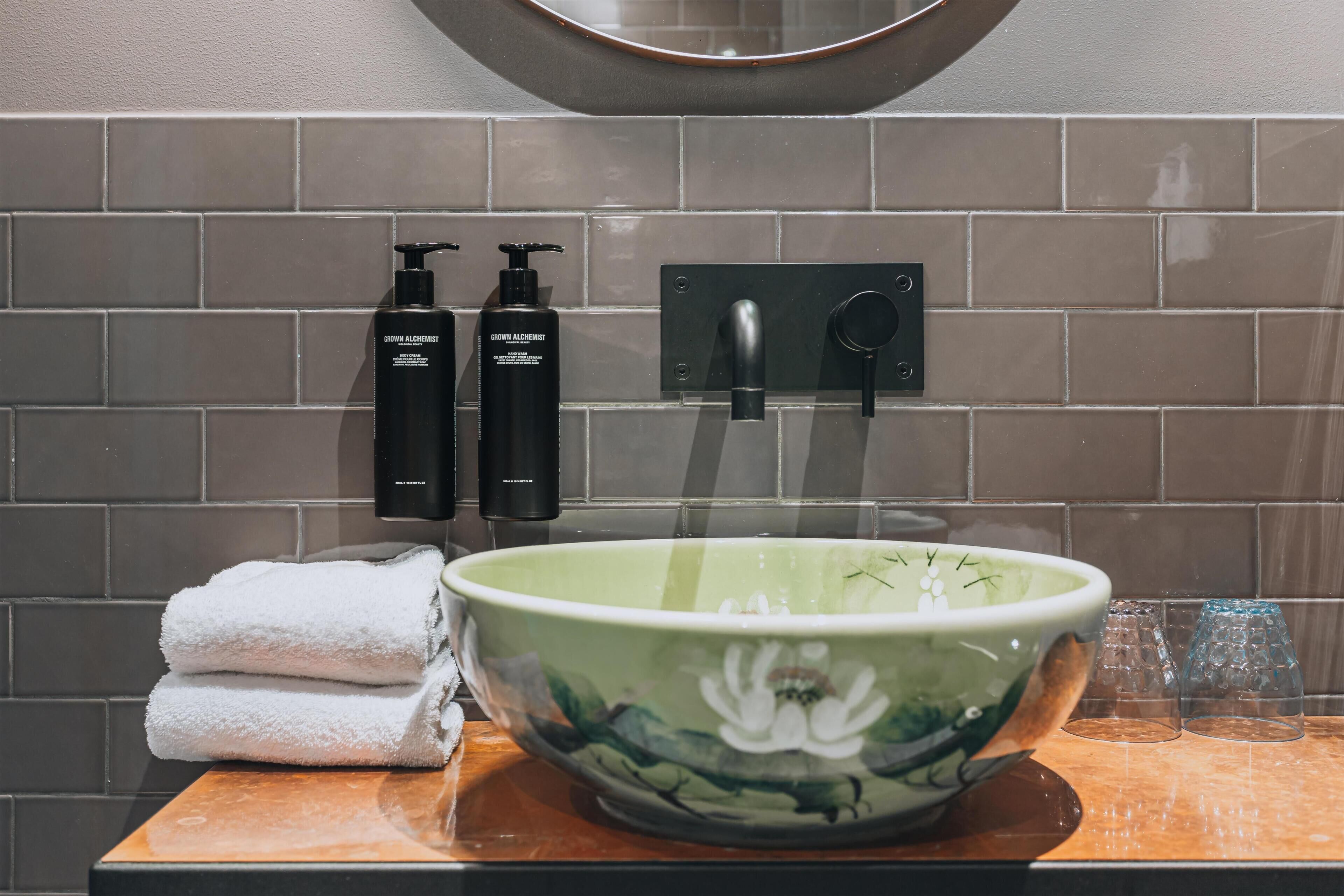 A bathroom with a green floral bowl, two black bottles, and a towel stack.