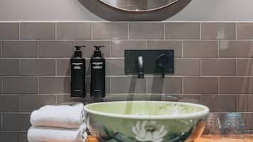 A bathroom with a green floral bowl, two black bottles, and a towel stack.