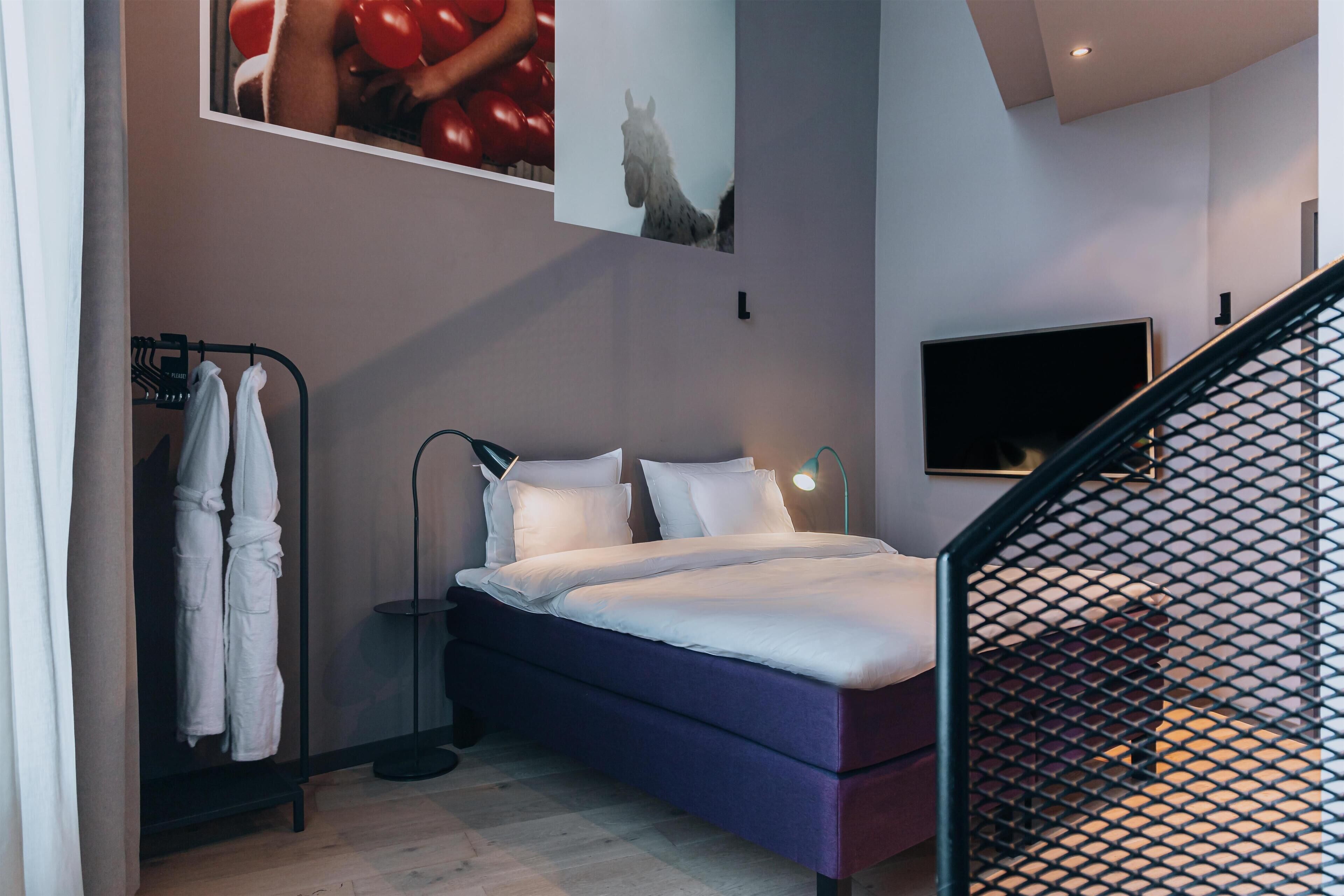 A modern bedroom with a bed, a TV, and a coat rack.
