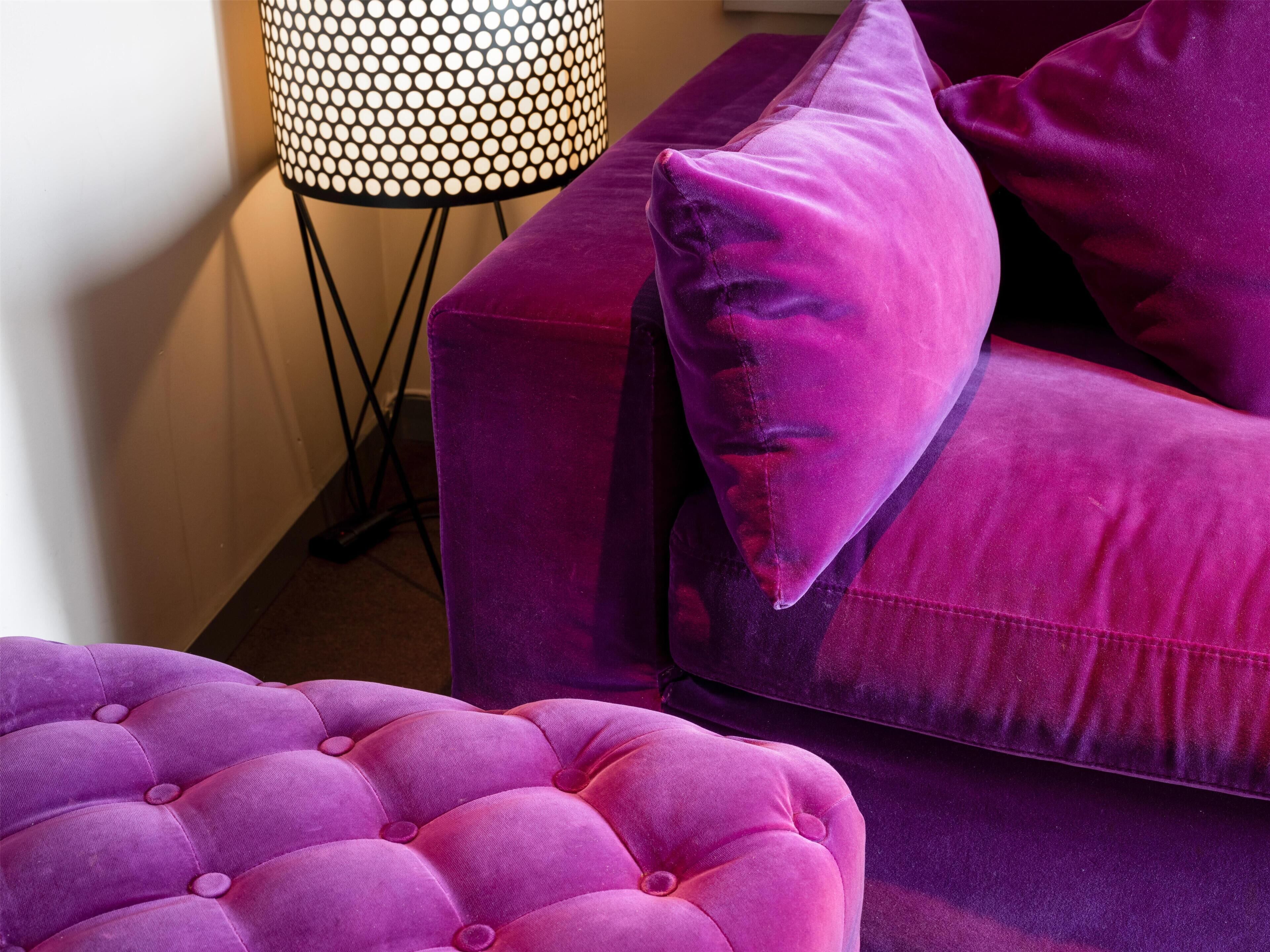 A purple sofa with a matching ottoman and a lamp with a circular pattern.