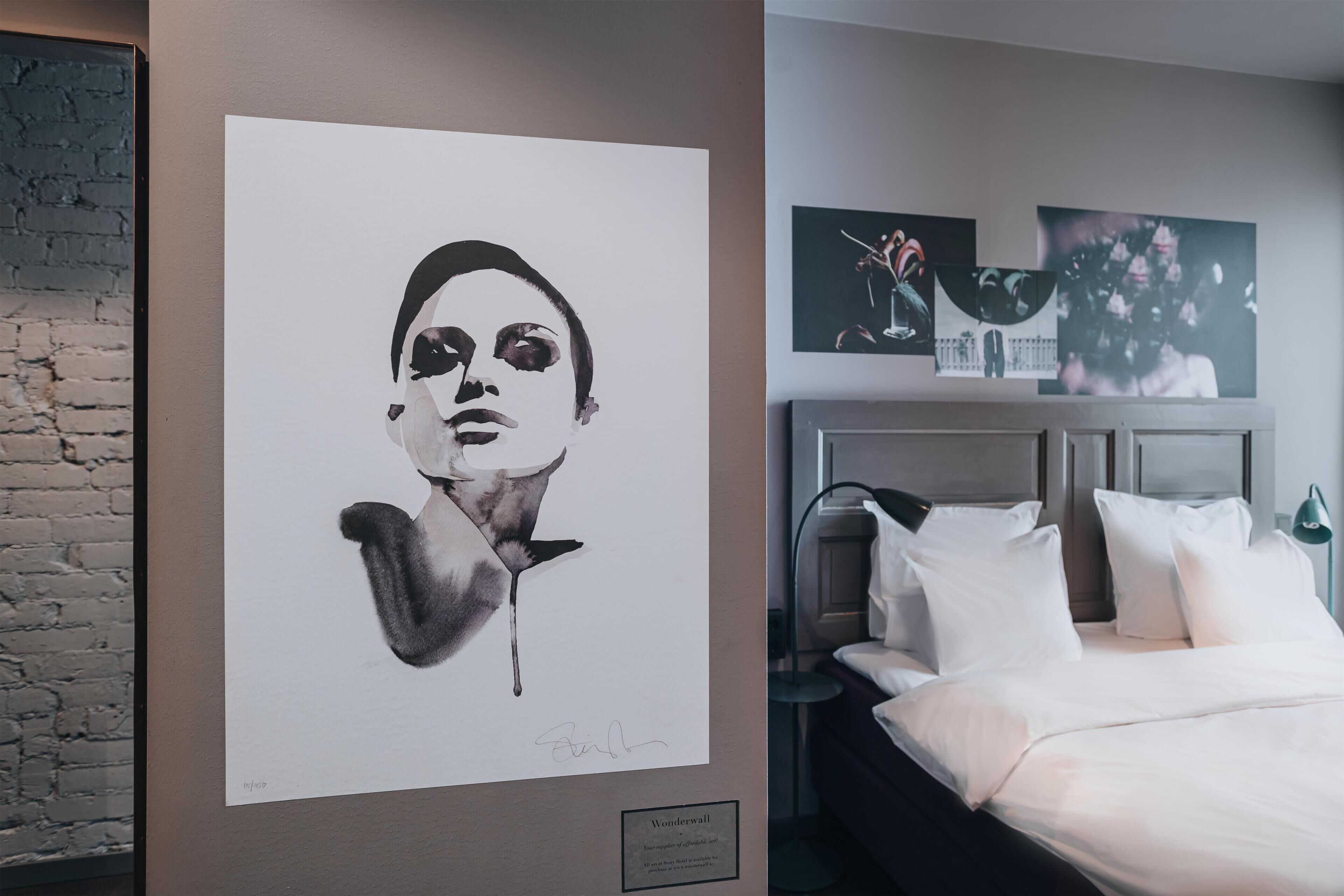 Quarto de hotel com cama, cabeceira, obra de arte pendurada na parede e parede de tijolos.