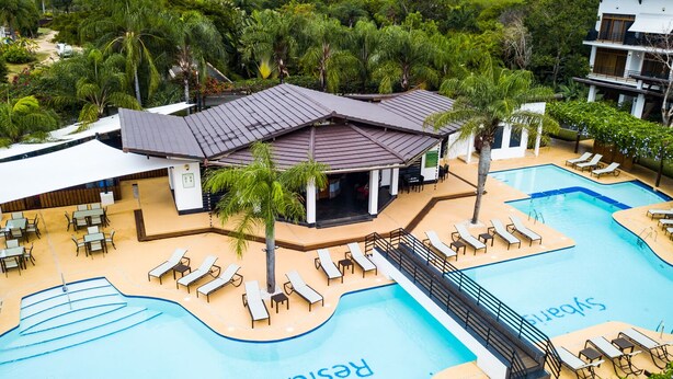 Un complexe hôtelier doté d’une piscine, de chaises longues et d’un espace abrité avec des tables et des chaises.