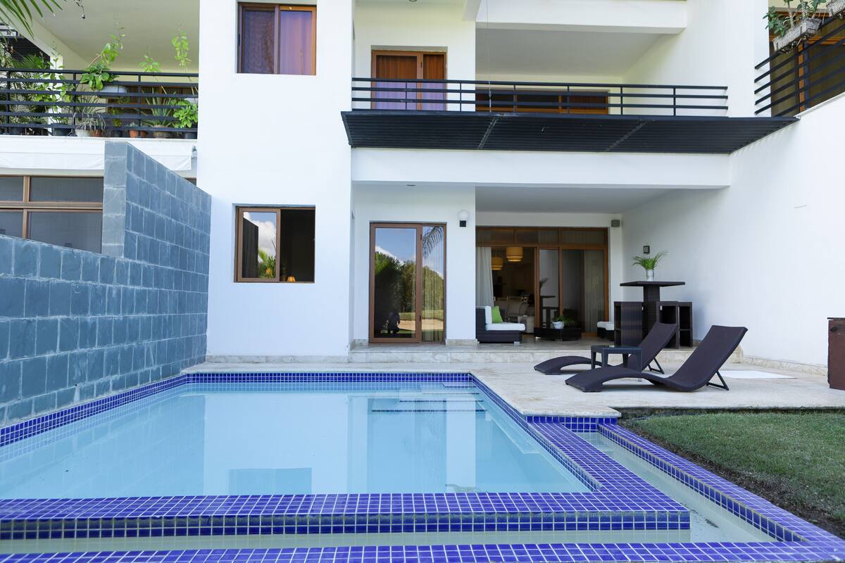A modern two-story house with a swimming pool, a balcony, and a patio area with lounge chairs.