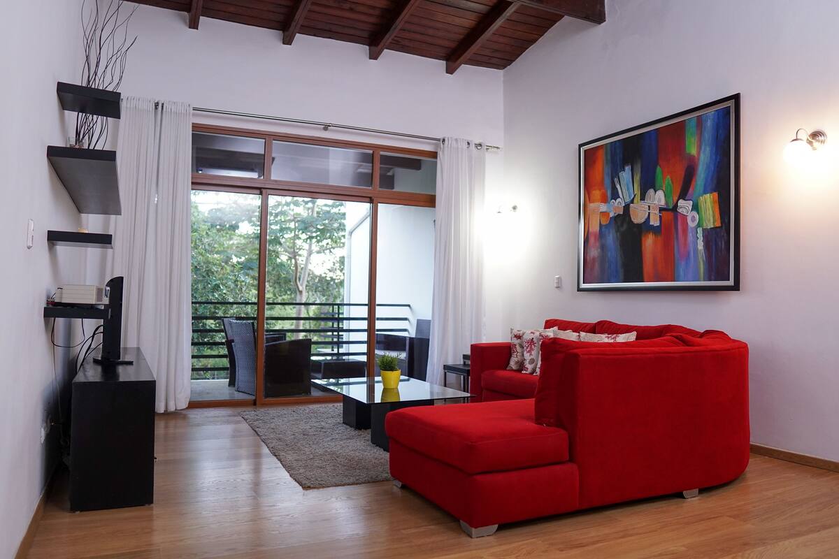 A modern living room with a red sofa, a glass coffee table, and a painting on the wall.