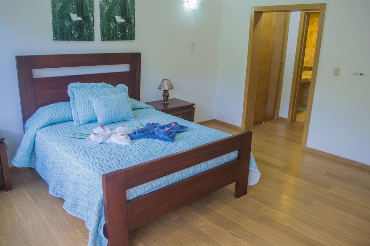 A bedroom with a wooden bed, a nightstand, a lamp, and a door leading to another room.