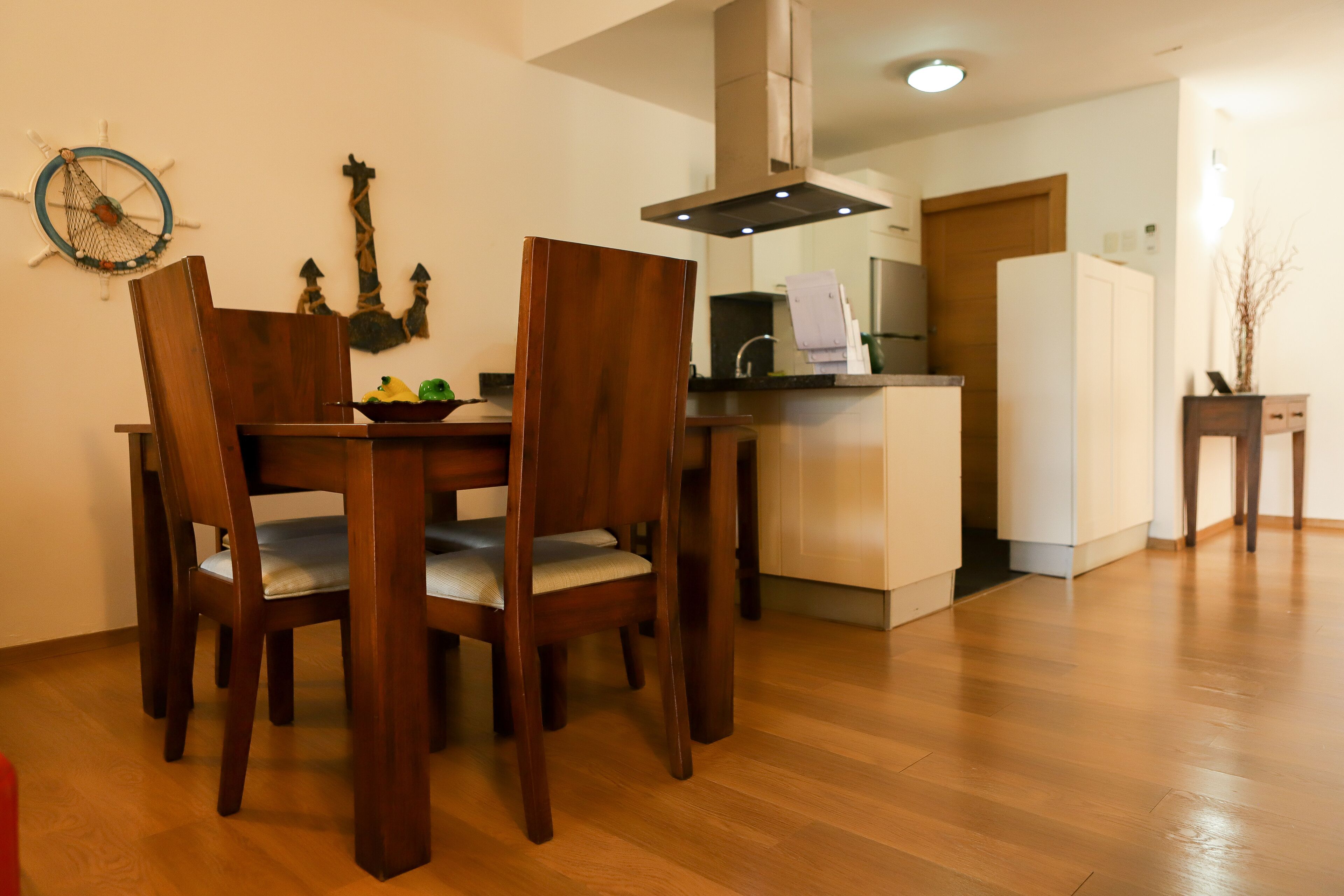 Un comedor con una mesa y sillas de madera, una cocina al fondo y piso de madera.