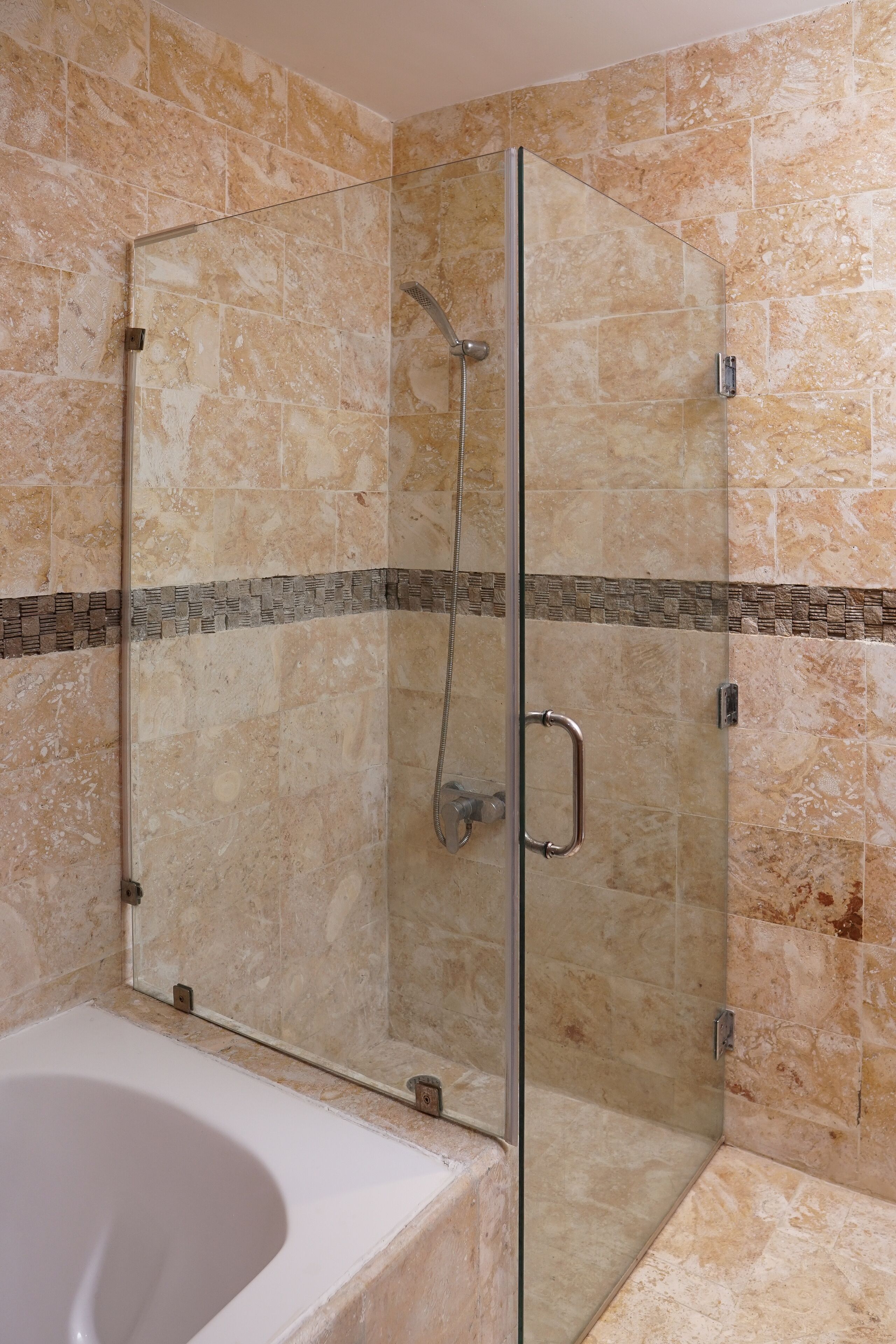 A glass-enclosed shower with a handheld showerhead and a glass door.