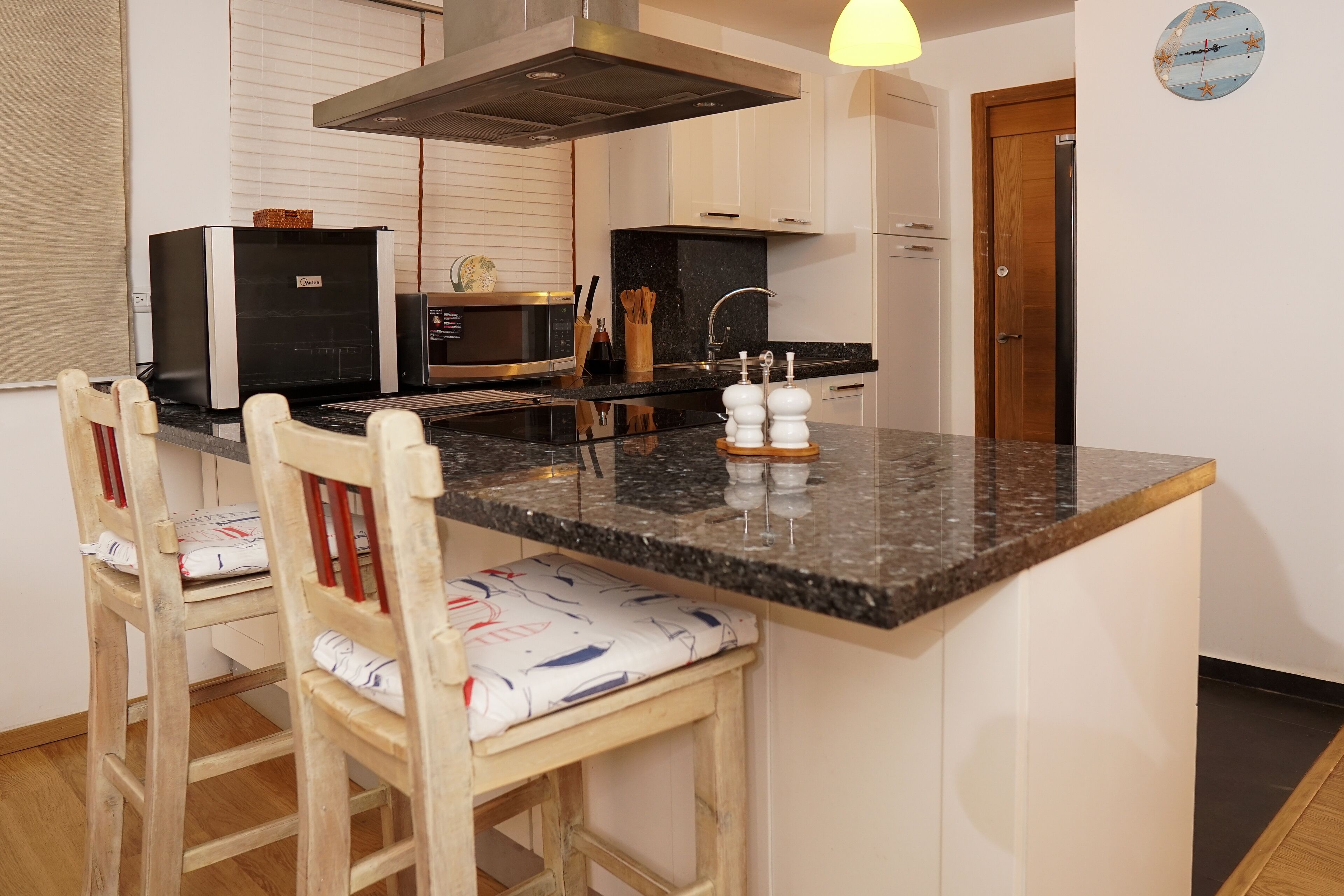A kitchen with a central island, a microwave, a stove, and a sink. There are two wooden chairs with cushions.