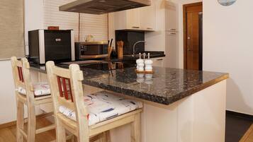 A kitchen with a central island, a microwave, a stove, and a sink. There are two wooden chairs with cushions.