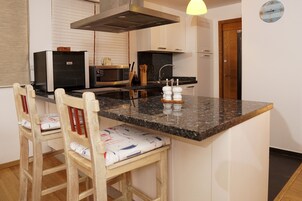 A kitchen with a central island, a microwave, a stove, and a sink. There are two wooden chairs with cushions.