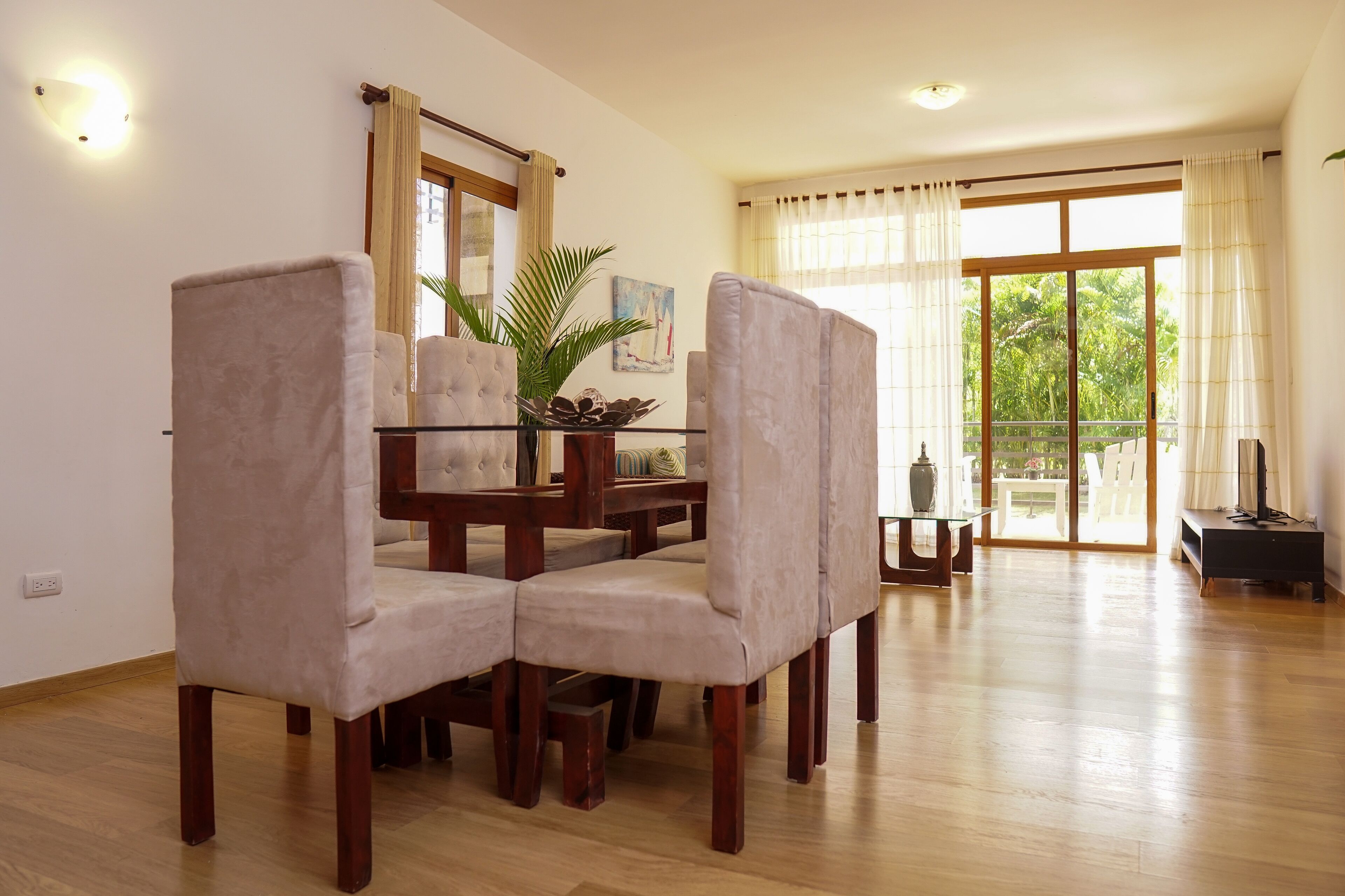 Un coin repas avec une table en bois et quatre chaises rembourrées, une plante en pot et un tableau accroché au mur.