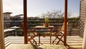 Un balcon avec une table et des chaises en bois, un pot de fleurs et une vue sur des immeubles et des arbres.