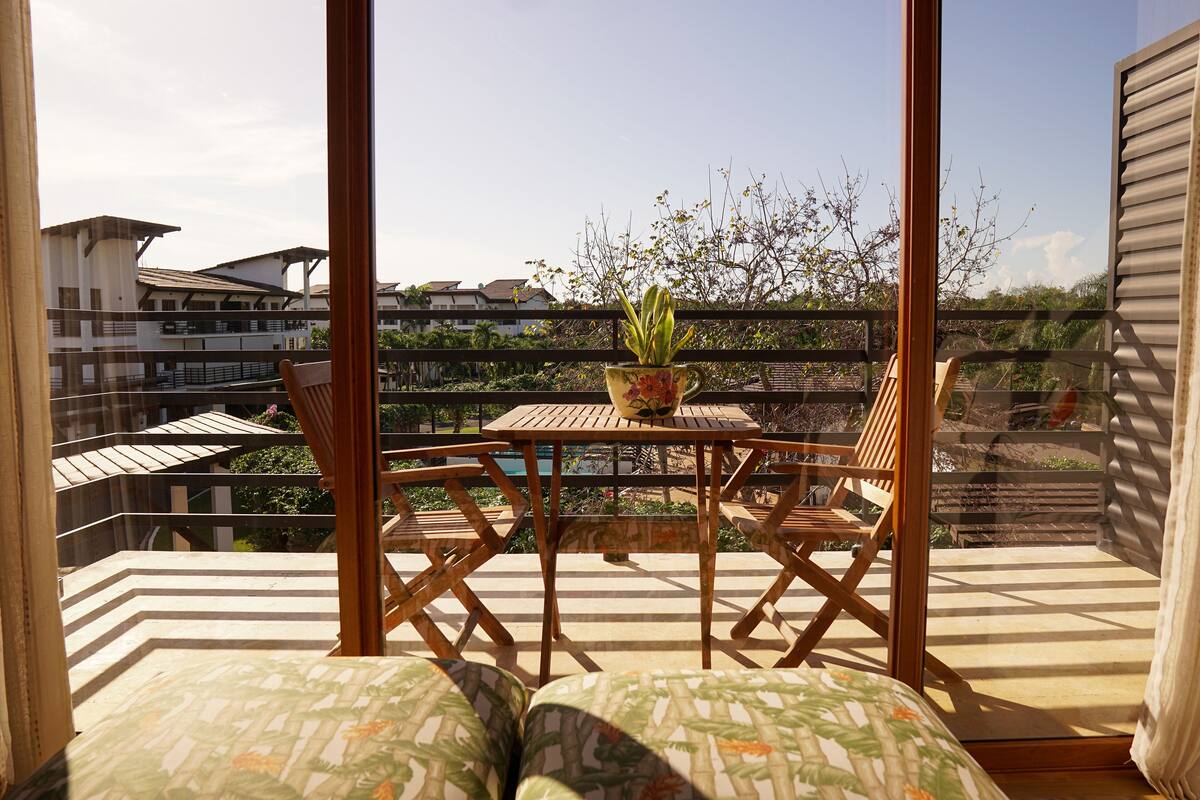 A balcony with a wooden table and chairs, a potted plant, and a view of buildings and trees.