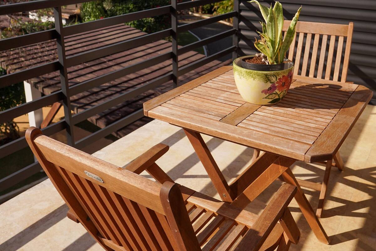 A wooden table and chairs on a balcony with a potted plant.