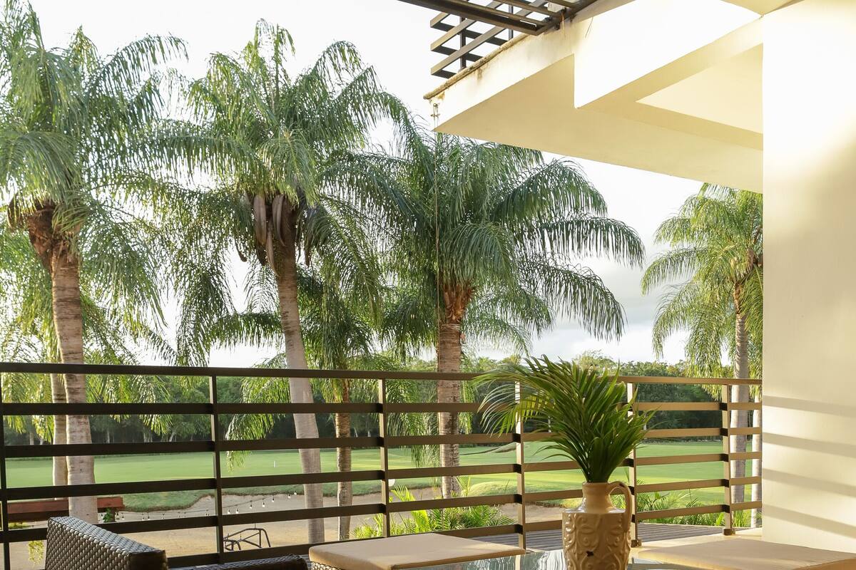A balcony with wicker furniture and a potted plant, overlooking a golf course.