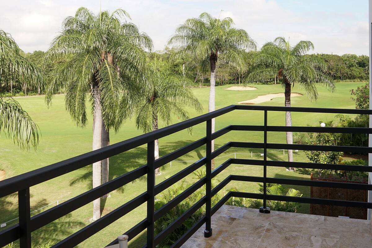 A balcony with a view of a golf course, palm trees, and a clear sky.