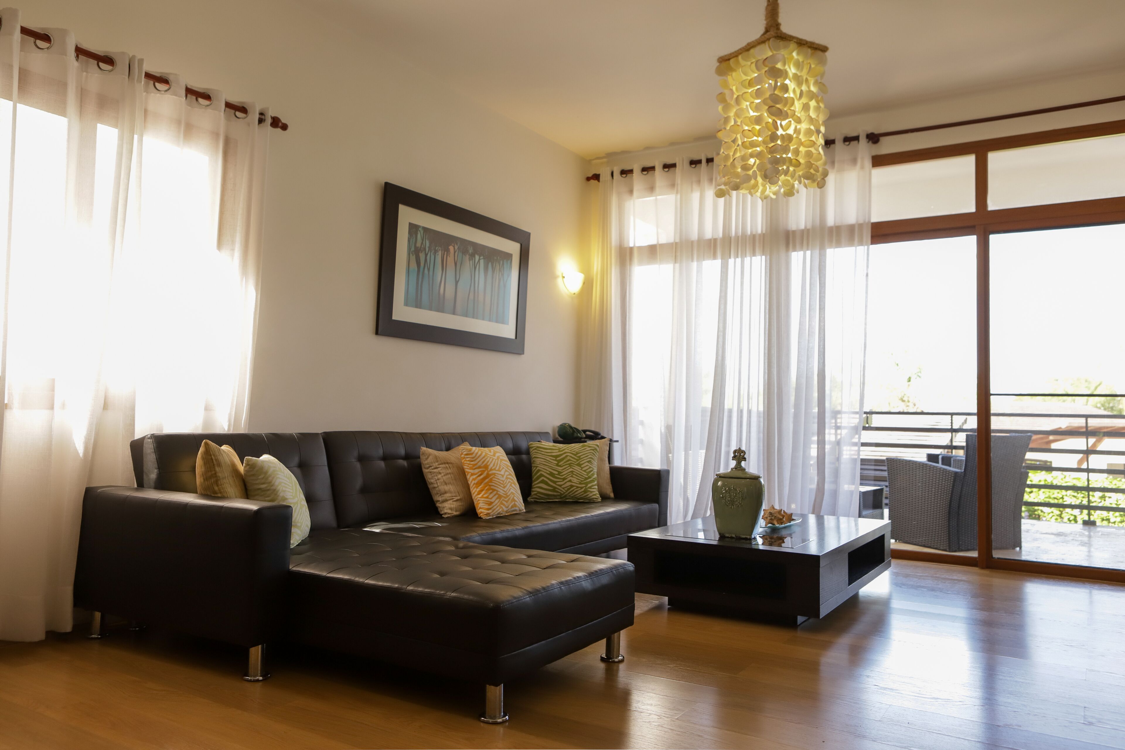 A modern living room with a sectional sofa, a coffee table, and a large window with sheer curtains.